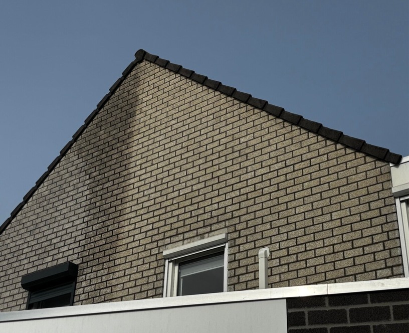 Resultaat na gevelreiniging: strakke, egale baksteengevel van een woning in Helmond onder een strakblauwe lucht.