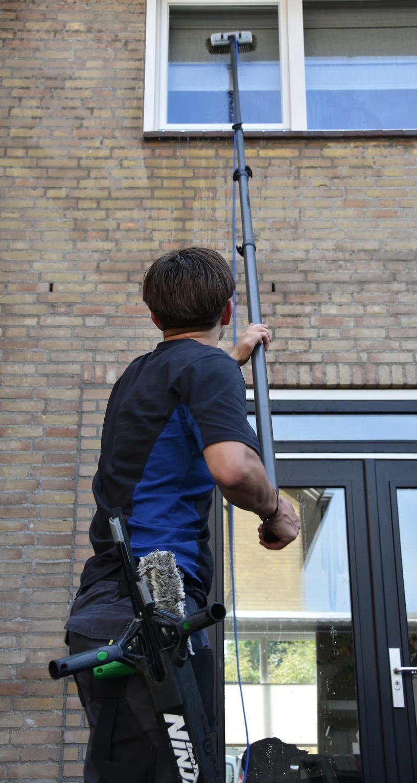 HGH-medewerker reinigt met een telescopische waterstok op zuiver water de ramen op de eerste verdieping van een woning in Helmond.